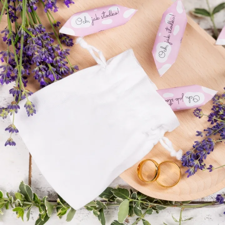 Elegant hvid satinpose ved siden af guldvielsesringe og lavendel.